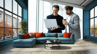 Two cheerful businessmen discussing something on the laptop in an office Wall mural